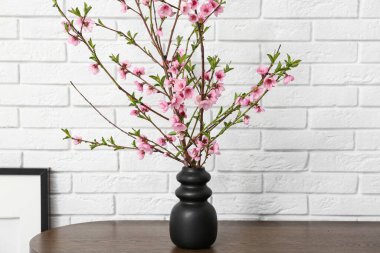 Oturma odasındaki beyaz tuğla duvarın yanında pembe çiçek açan vazolardan oluşan bir elbise.