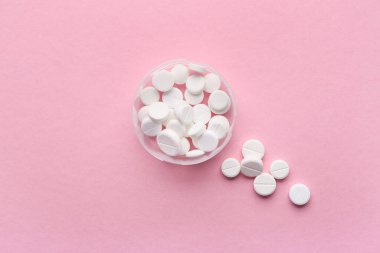 Pembe arka planda beyaz haplarla dolu bir kap.