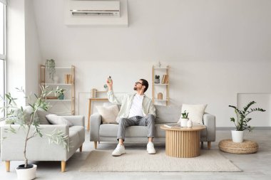 Genç adam oturma odasında klimayı açıyor.