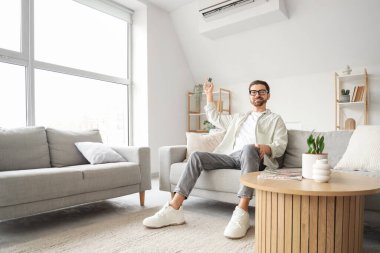 Genç adam oturma odasında klimayı açıyor.