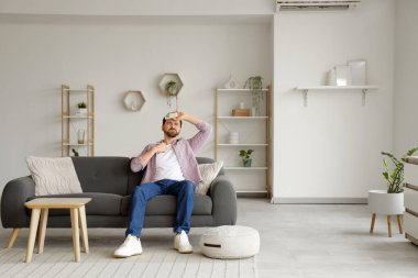 Klima kumandalı genç adam oturma odasındaki kanepede sıcaktan acı çekiyor.