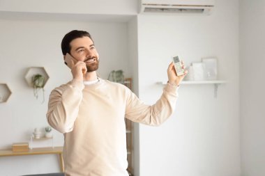 Klimalı genç adam evde cep telefonuyla konuşuyor.