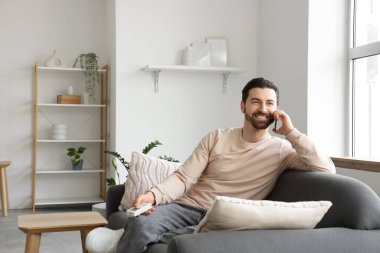 Evdeki klimanın yanındaki kanepede cep telefonuyla konuşan genç adam.