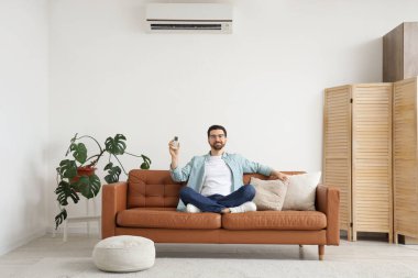 Klimalı yakışıklı bir adam oturma odasındaki kanepede oturuyor.