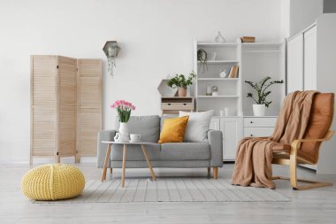 İçinde gri kanepe, vazoda laleler ve bitkiler olan oturma odasının içinde.