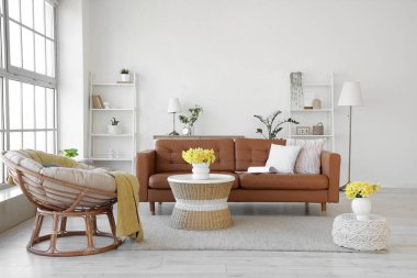 Oturma odasının içinde kahverengi kanepe, koltuk ve vazolarda nergis.