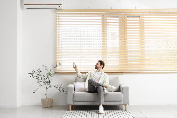 Красивый мужчина включает кондиционер с дивана в гостиной