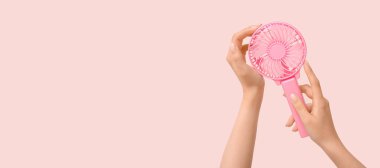 Pembe arka planda mini fanı olan genç bir kadının elleri.