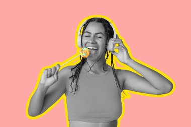 Lolipopu olan mutlu Afro-Amerikalı kadın pembe arka planda müzik dinliyor.
