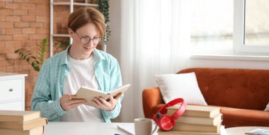 Gözlüklü erkek öğrenci evde kitap okuyor.