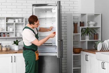 Mutfaktaki buzdolabını tamir eden mutlu erkek işçi.