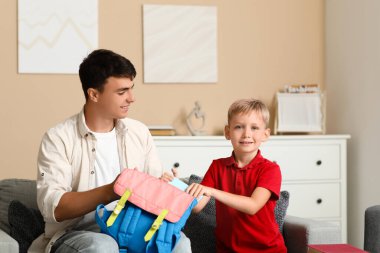 Baba ve küçük oğlu evde sırt çantalarına kitap dolduruyorlar.