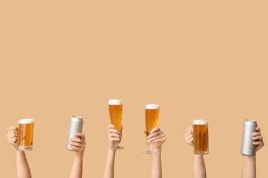 Teneke kutularda taze bira, bardaklarda ve kupalarda bej arka planda kadın eli.