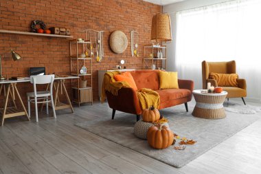 Oturma odasında rahat bir kanepe, koltuk, sehpa ve sonbahar dekoru var.