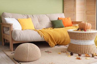 Oturma odasının içinde sonbahar dekoru olan rahat bir kanepe ve kahve masası.