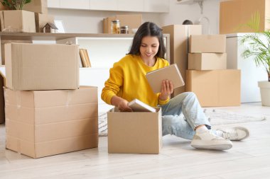 Güzel bir kadın taşınma gününde kitapları mutfaktaki kutuya koyar.