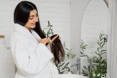 Genç hamile bir kadın banyoda saç uzatmak için serum kullanıyor.