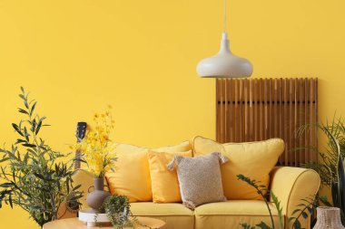 Sarı kanepe ve yeşil bitkilerle dolu oturma odasının içinde.