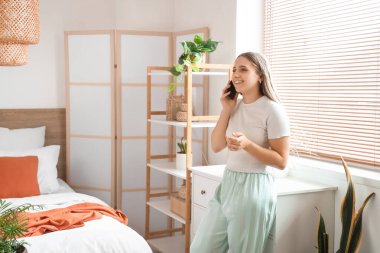 Modern yatak odasında cep telefonuyla konuşan güzel genç bir kadın.