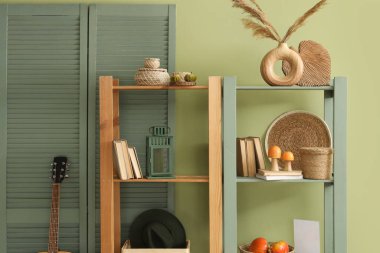 Yeşil duvarın yanında balkabağı, mantar, kitap ve dekor olan raf ünitesi