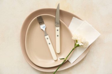 Çatal bıçaklı tabaklar, kağıt peçeteler ve bej grunge arka planda karanfil.