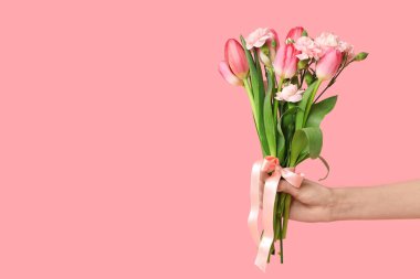 Pembe arka planda Anneler Günü için bir buket güzel bahar çiçeğiyle bir kadın eli.