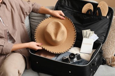 Şapkalı genç bir kadın evdeki koltukta seyahat etmek için bavul hazırlıyor.