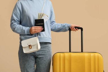 Çantası, pasaportu ve bej rengi geçmişi olan genç bir kadın.