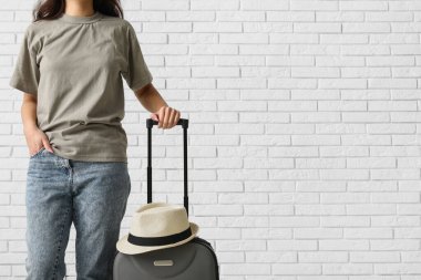 Beyaz tuğla arka planda bavulu ve şapkası olan genç bir kadın.