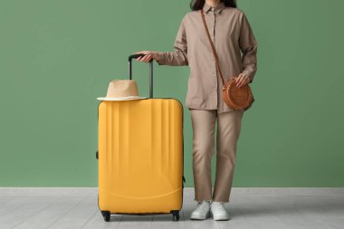 Çantalı, çantalı ve şapkalı genç kadın yeşil duvarın yanında.