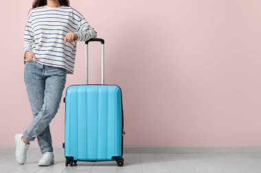 Pembe duvarın yanında bavulu olan genç bir kadın.