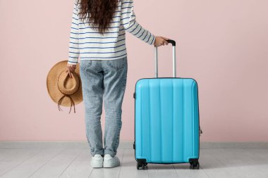 Pembe duvarın yanında bavulu ve şapkası olan genç bir kadın.
