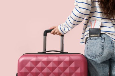 Çantası, pasaportu ve pembe arka planda biletleri olan genç bir kadın.
