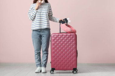 Pembe duvarın yanında bavulu, seyahat yastığı ve pasaportu olan genç bir kadın.