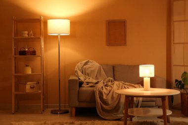 Gece oturma odasının içinde kanepe, raf ünitesi, parlayan lambalar ve kahve masası.