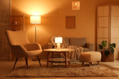 Gece oturma odasının içinde kanepe, koltuk, parlayan lambalar, katlanır ekran ve kahve masası.