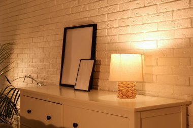 Beyaz tuğla duvarın yanında parlayan lamba ve resimlerle dolu bir oturma odası.