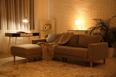 Gece oturma odasının içinde kanepe, raf ünitesi, parlayan lambalar ve işyeri