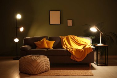 Gece oturma odasının içinde, kanepe, puf ve yeşil duvarın yanında parlayan lambalar.