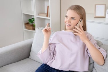 Evdeki koltukta cep telefonuyla konuşan genç sarışın kadın.