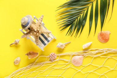 Sarı arka planda deniz kabukları, ağ ve palmiye yapraklı dekoratif şezlong.