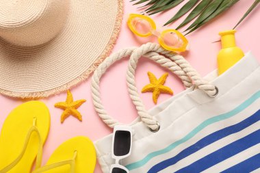 Terlikli şapka, plaj çantası ve pembe arka planda yüzme gözlüğü.