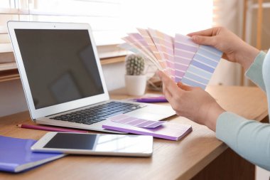 Dizüstü bilgisayarı, tablet bilgisayarı ve boya palet kumaşlı genç bir kadın. Evdeki masanın yanında leylak rengi seçiyor. Yakın plan.