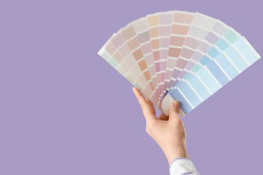 Leylak arka planında boya paleti örnekleri olan bir kadın el.