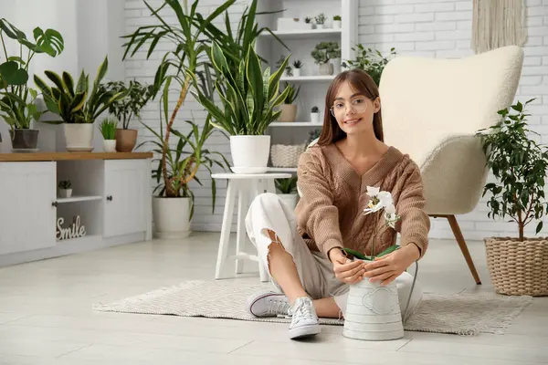 Genç bayan bahçıvan, saksının yanında, evinde çiçekle oturuyor.