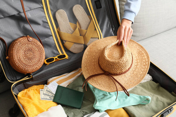 Young woman with hat packing suitcase for travel on sofa at home, closeup