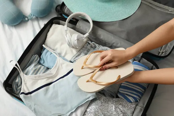 Parmak arası terlikleri olan genç bir kadın evde seyahat etmek için bavulunu hazırlıyor, yakın plan.
