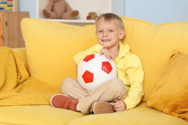 Futbol topuyla sarı koltukta oturan sevimli küçük çocuk.