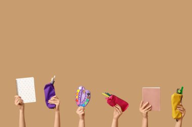 Boya paleti tutan kadın eller, not defterleri ve bej arka planda kırtasiye malzemesi olan kalem kılıfları.