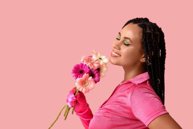 Pembe arka planda saçları ve çiçekleri olan şık bir Afro-Amerikalı kadın.